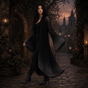May include: A long, black, hooded crochet cardigan featuring an open-front design, long flared bell sleeves, and a detailed, intricate knit pattern throughout the garment. The cardigan extends to the lower calf and is worn over black trousers.