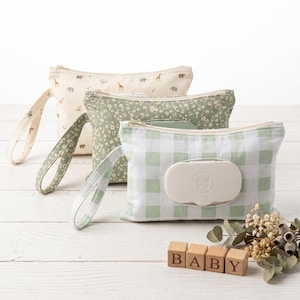 Può includere: Tre pochette per salviette per bambini con diversi motivi: una pochette color crema con stampa animalier, una pochette con stampa floreale verde e una pochette a quadri verdi e bianchi. Ogni pochette ha un manico abbinato e una chiusura a zip.