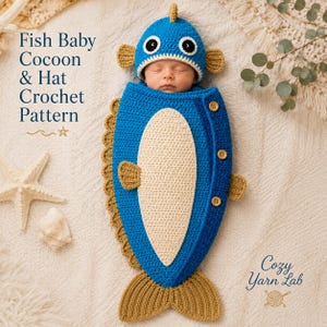 May include: A blue and beige crochet fish baby cocoon and matching hat. The cocoon features a cream-colored belly, brown fins, and a brown tail. Three wooden buttons secure the side. Text reads: Fish Baby Cocoon & Hat Crochet Pattern, Cozy Yarn Lab.