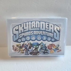 May include: A clear plastic case featuring the game title "Skylanders Spyro's Adventure" in blue and white lettering. The case displays various cartoon characters and game symbols. The case is rectangular and sits on a white surface.