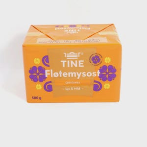 Puede incluir: Caja naranja de TINE Fløtemysost, un producto lácteo noruego. El embalaje presenta diseños florales morados y el texto "TINE Fløtemysost ORIGINAL - Lys & Mild". La caja contiene 500 g de producto.