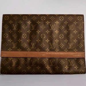 May include: Brown clutch with a repeating pattern of interlocking logos and floral designs. A horizontal band of brown leather is across the middle. The clutch is rectangular and appears to be made of leather.