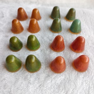 Puede incluir: Una variedad de pequeños objetos en forma de cono en varios colores, incluyendo tonos de naranja, verde y marrón. Los objetos tienen un acabado liso y brillante y están dispuestos sobre una superficie blanca texturizada. Artículos decorativos o funcionales.