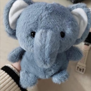 May include: A plush blue elephant toy with large ears and a long trunk. The elephant has black button eyes and a soft, furry texture. The inside of the ears are white.