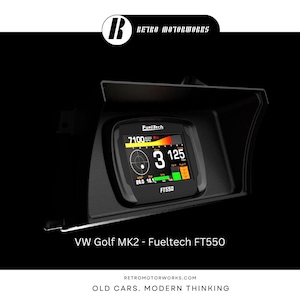 May include: Black dashboard display with a digital screen showing RPM, speed, and other data. The screen displays the text "FuelTech" and "FT550". The display is mounted in a black housing. The text "VW Golf MK2 - Fueltech FT550" is below the display.