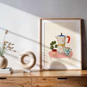 Puede incluir: Una impresión artística enmarcada que presenta una naturaleza muerta con una cafetera, tazas y una planta sobre una mesa rosa. La cafetera tiene un asa roja y una tapa azul. Las tazas tienen patrones coloridos. La impresión se muestra en un mueble de madera.
