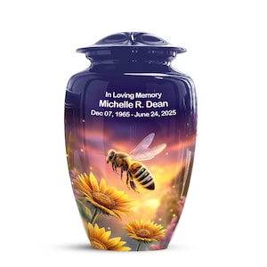 May include: A navy blue cremation urn with a bee and sunflower design. The urn has the text "In Loving Memory Michelle R. Dean Dec 07, 1965 - June 24, 2025". The background features a sunset.