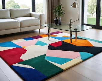 May include: A colorful geometric area rug with a modern design. The rug features a patchwork of shapes in red, blue, green, pink, orange, and black against a white background. The rug is placed on a hardwood floor in a living room setting.