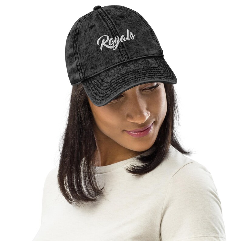 May include: A black, distressed baseball cap with the word "Royals" embroidered in white script. The cap has a curved brim and a classic six-panel design. The hat is worn by a person.