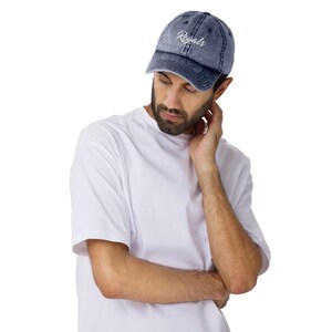 May include: A denim blue baseball cap with the word "Royals" embroidered in white script. The cap has a curved brim and a distressed, vintage look. The cap is worn by a person wearing a white t-shirt.