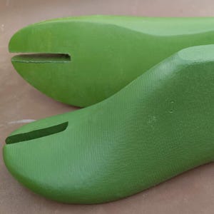Puede incluir: Dos hormas de zapatos verdes, una en primer plano y otra en segundo plano. Las hormas de zapatos están hechas de un material sólido y tienen una forma lisa y curvada. Cada una tiene una ranura en la puntera y una pieza metálica en el talón.