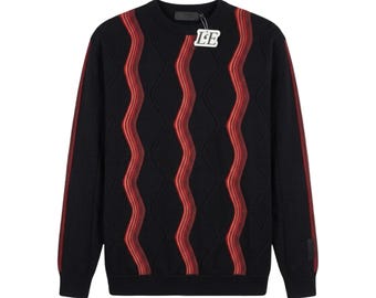 May include: Black crew neck sweater with red wavy stripes and diamond pattern. The sweater has long sleeves with red stripes down the sides. A tag with the letters "LE" is attached to the sweater.