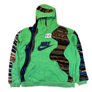 Op de afbeelding: Groene Nike hoodie met een voorzak en een capuchon. De hoodie heeft een groot marineblauw Nike logo en patchwork ontwerpen in verschillende kleuren en patronen. Een klein label met de letters "LE" is bevestigd.