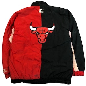 May include: A red and black Chicago Bulls Starter jacket. The jacket features a split design with the team's logo prominently displayed on the back. The Starter logo is visible on the upper left chest. The jacket has a zip-up front and a stand-up collar.