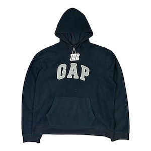Może przedstawiać: Granatowa bluza z kapturem z napisem "GAP" w dużych, szarych literach na piersi. Słowo "LE" znajduje się nad logo "GAP". Bluza ma przednią kieszeń i kaptur ze sznurkiem.