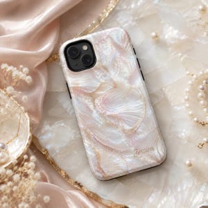 Op de afbeelding: Een parelmoeren telefoonhoesje met een wervelend, schelpachtig ontwerp in tinten roze, wit en goud. De hoes heeft een zwarte rand en de naam "Jessica" is in gouden letters gegraveerd. De telefoonhoes ligt op een wit oppervlak.