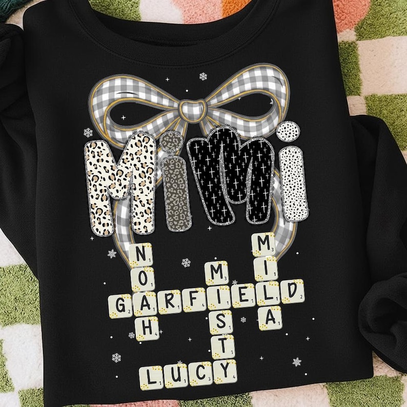 May include: Black sweatshirt with the word "Mimi" in a decorative font, with a bow design above. The letters are decorated with leopard print, glitter, and polka dots. Below, a crossword puzzle spells out names.