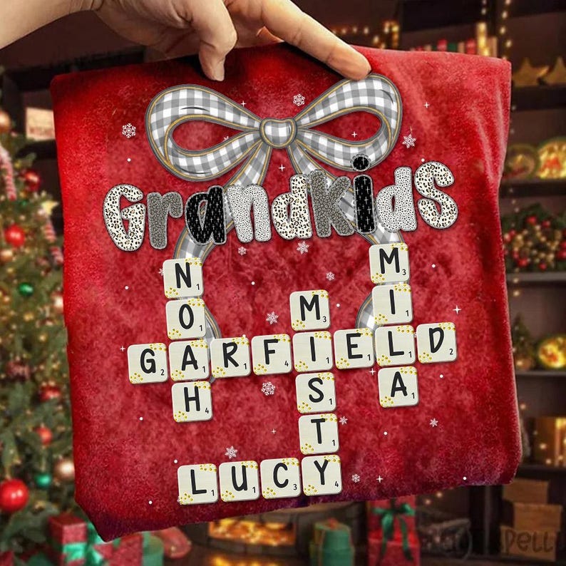 May include: A red decorative pillow with the word "Grandkids" in a mix of patterned fonts. Scrabble tiles spell out names like "Garfield" and "Lucy". A gray and white plaid bow and snowflakes add to the festive design.