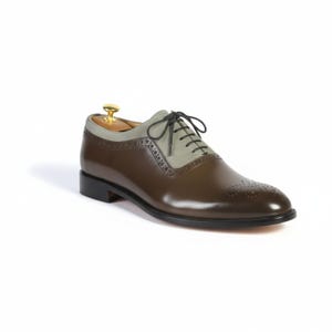 Two-tone men's dress shoes combining brown leather and grey suede with traditional oxford lacing and brogue accents. Artisan-crafted formal shoes with elegant contrast on white background.