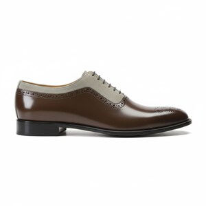 Men's luxury brown and grey oxford shoes featuring polished leather toe, cream suede panels, and decorative perforations. Handcrafted formal shoes with vintage styling on white surface.