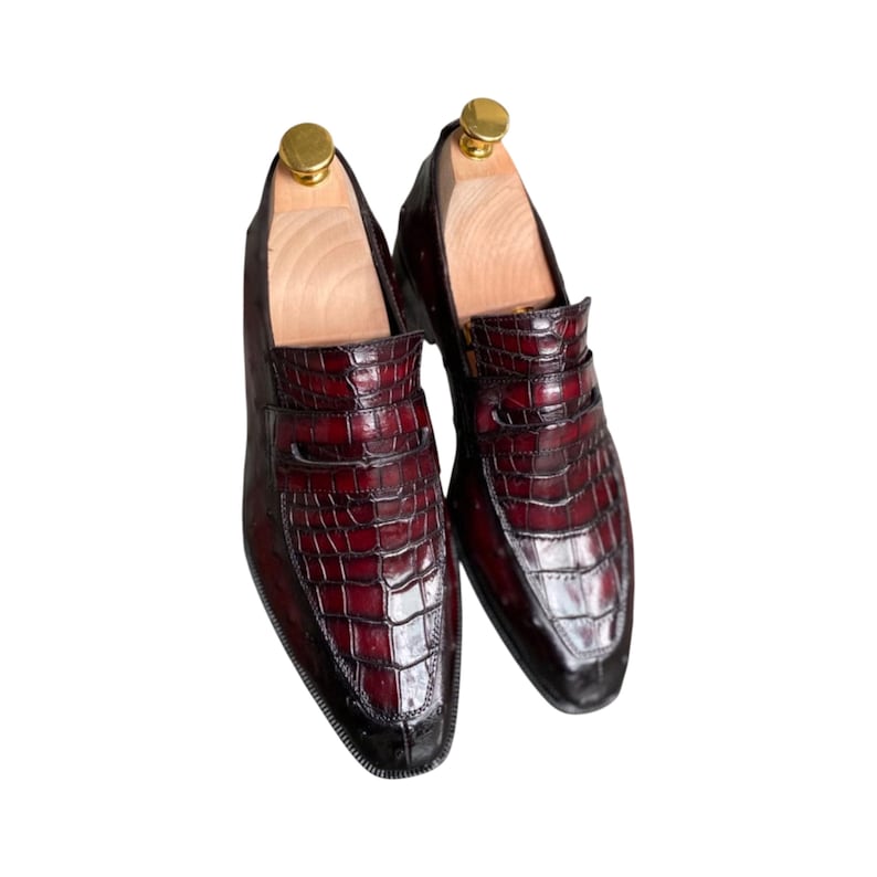 Men's wine red slip-on loafers with crocodile embossed leather and gold metal bar accent. Handmade formal dress shoes with pointed toe. Ideal for business executives, formal events, luxury occasions, or distinguished gentleman's wardrobe.