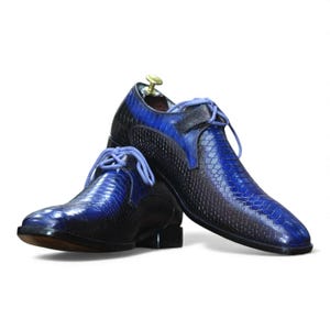 Peut inclure: Paire de chaussures de ville en cuir bleu et noir avec un motif peau de serpent texturé. Les chaussures ont des lacets bleus et un petit talon. Le design présente un dégradé de nuances de bleu, créant un look élégant et sophistiqué.