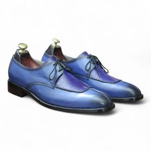 May include: A pair of blue leather dress shoes with black laces. The shoes have a two-tone design, with a darker blue vamp and a lighter blue body. The soles and heels are black. The shoes are on shoe trees.