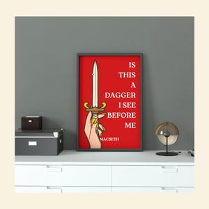 May include: A framed art print with a red background features a hand holding a dagger. The text reads "IS THIS A DAGGER I SEE BEFORE ME" with "MACBETH" below. The print is in a black frame.