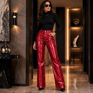 Puede incluir: Un suéter de cuello alto negro de manga larga combinado con pantalones de cintura alta y pierna ancha con un patrón de piel de serpiente rojo brillante. Los pantalones incluyen cierre de botón frontal, trabillas y bolsillos laterales.
