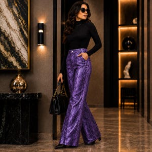 May include: A long-sleeved black turtleneck top paired with high-waisted, wide-leg trousers featuring a purple and black snakeskin pattern. The trousers have a button closure and side pockets. A black handbag with a gold chain strap is held.