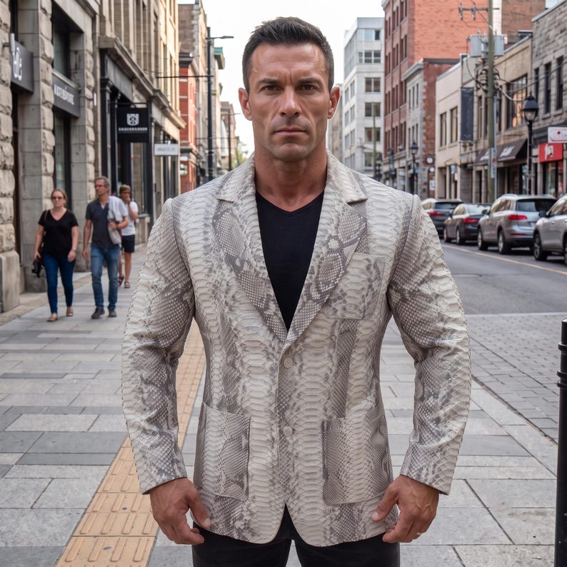 May include: A blazer featuring a light grey and white snakeskin pattern with a notched lapel, two front patch pockets, and a two-button closure. The garment is worn over a solid black v-neck shirt, showcasing long sleeves and a structured fit.