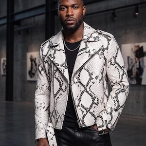 May include: A white and black snakeskin print motorcycle jacket featuring a notched lapel, silver-tone metal zippers, a waist belt with a buckle, and long sleeves with zippered cuffs, worn over a plain black shirt with a silver chain necklace.