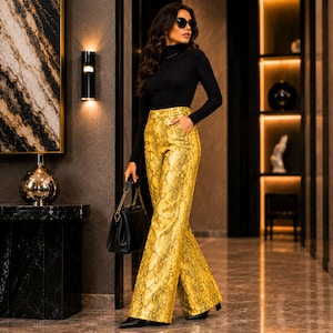 Op de afbeelding: Een zwart shirt met lange mouwen en een col, gecombineerd met een gele broek met hoge taille en een slangenprint. De broek heeft wijde pijpen en zijzakken. Een zwarte handtas met een gouden ketting als schouderband wordt vastgehouden.