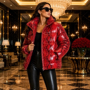 May include: A glossy red puffer jacket featuring a black snakeskin pattern, a high collar, and a full-length front zipper. The jacket is worn over a black top and black leather-style pants, paired with dark-tinted sunglasses.