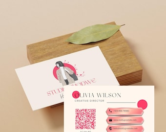 Puede incluir: Tarjetas de visita con fondo rosa claro y una ilustración de mujer en un círculo rojo. Las tarjetas incluyen el nombre "Olivia Wilson", información de contacto y un código QR. Un bloque de madera y una hoja también están en la imagen.