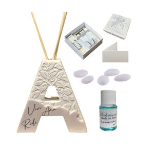 Può includere: Un diffusore in ceramica bianco sporco a forma di lettera "A" con dettagli floreali e le parole "Vivi Ama Ridi". Include una piccola bottiglia di olio alla lavanda, una confezione regalo e confetti.