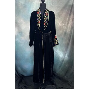 May include: A long, black velvet robe with floral embroidery in red, gold, and green. The robe features a shawl collar, a matching belt, and gold trim along the edges. The embroidery is concentrated on the collar and cuffs.