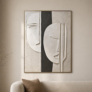 Puede incluir: Arte mural abstracto con dos rostros estilizados en relieve, enmarcado en dorado. La obra utiliza una paleta de colores neutros con tonos blancos, negros y beige. Una franja vertical negra divide los rostros.