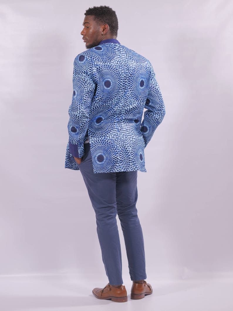 Puede incluir: Una chaqueta azul con un dise&ntilde;o estampado blanco y azul. La chaqueta tiene un cuello mandar&iacute;n y mangas largas. La persona lleva pantalones azules y zapatos marrones.