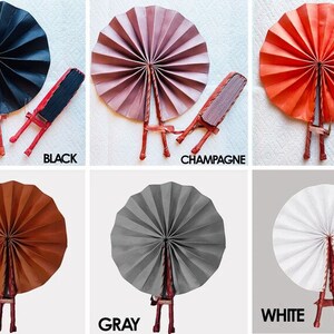 May include: Six hand fans in different colors: black, champagne, orange, brown, gray, and white. Each fan is made of paper and has a wooden handle. The fans are arranged in a grid pattern.