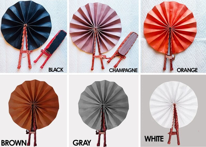 May include: Six hand fans in different colors: black, champagne, orange, brown, gray, and white. Each fan is made of paper and has a wooden handle. The fans are arranged in a grid pattern.