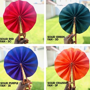 May include: Four hand fans, each a different solid color: red, green, purple, and orange. The fans are made of paper and have a wooden handle.