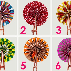May include: Six colorful, patterned hand fans on wooden stands. The fans feature various designs, including geometric and floral patterns in red, blue, yellow, green, orange, and pink. Each fan is numbered 1 through 6.