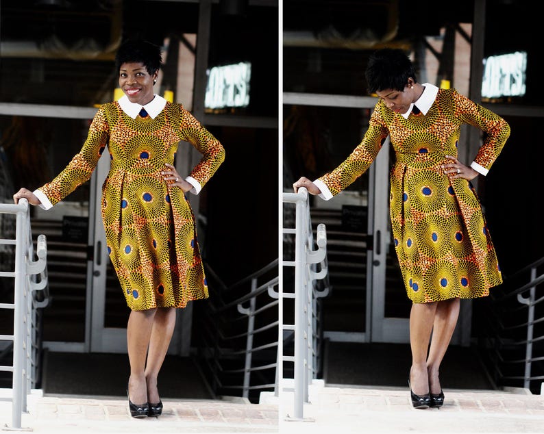 May include: A woman wearing a yellow and blue patterned dress with a white collar and long sleeves. She is standing on a set of stairs with a railing.