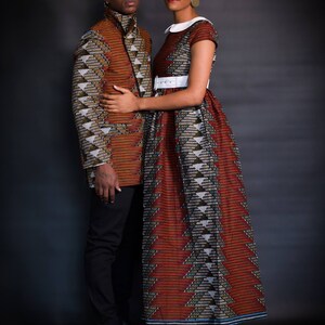 K&ouml;nnte beinhalten: Ein Paar tr&auml;gt passende gemusterte Outfits. Die Frau tr&auml;gt ein rot-schwarzes Kleid mit einem wei&szlig;en G&uuml;rtel und einem wei&szlig;en Kragen. Der Mann tr&auml;gt eine braun-schwarze Jacke mit einem &auml;hnlichen Muster. Sie stehen vor einem dunklen Hintergrund.