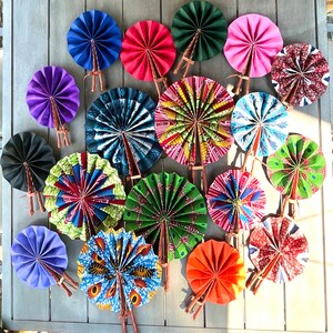 May include: A collection of colorful hand fans with various patterns and designs. The fans are made of paper and have wooden handles. The fans are arranged in a circle on a wooden surface.