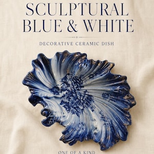 May include: A decorative ceramic dish with a shell-like, ruffled form, featuring a deep blue and white floral pattern with gold-toned accents along the edges. The text reads: WILLOW & WREN VINTAGE, SCULPTURAL BLUE & WHITE, DECORATIVE CERAMIC DISH, ONE OF A KIND.