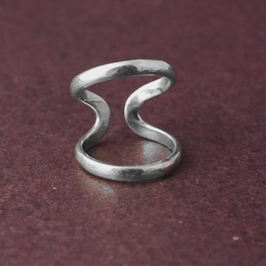 Può includere: Un anello color argento con un design unico a doppia fascia. L'anello presenta una forma ondulata e aperta, creando un look moderno ed elegante. Il metallo ha una finitura lucida, che riflette la luce. Questo gioiello è adatto all'uso quotidiano.