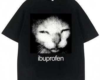 May include: A black short-sleeve t-shirt featuring a square graphic on the chest. The graphic displays a high-contrast, grainy black and white image of a cat's face. Below the cat image, the word ibuprofen is printed in white lowercase text.