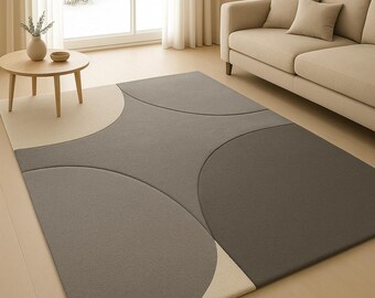 May include: A contemporary rug with a geometric pattern in grey and beige. The rug features large, overlapping circular shapes, creating a modern design. The rug is placed in a living room setting with a sofa and a small table.